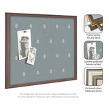 Rectangular pinboard with blue fabric featuring a repeating small white botanical pattern, framed in dark wood, displaying two black-and-white photos pinned on it.