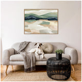 Abstract landscape wall art in muted greens and browns above a light gray sofa with a gray throw, round beige pillow, black wireframe coffee table, and a dog sitting on the sofa.