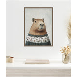 Framed canvas painting of a capybara wearing a blue and white sweater with snowflake patterns, set against a lightly snowy gray background.