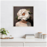 Framed canvas portrait of a woman with a large white flower obscuring her face, displaying soft beige and green tones against a dark background, hung above a white cabinet with plants and books.