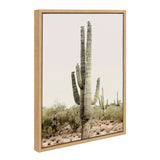 Framed canvas print of a tall multi-arm saguaro cactus in a desert landscape with shrubs under a pale sky, with a light wood frame.