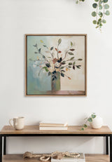 Framed botanical canvas depicting a bouquet of stylized leaves and flowers in muted blue, green, and beige tones, centered above a wooden table with neutral décor.