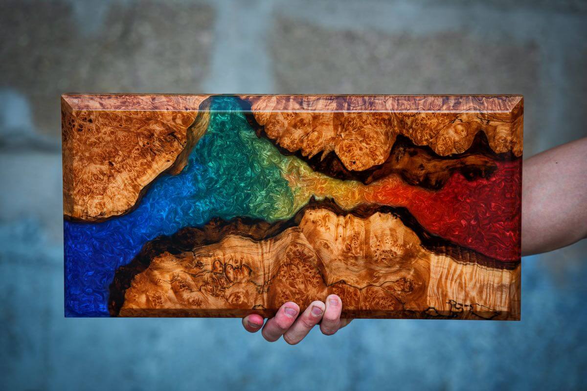 Hand holding a wooden panel with a rainbow design against a blurred background