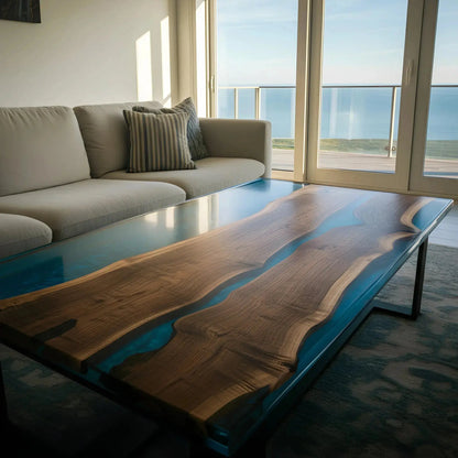 Custom epoxy river coffee table with sculpted walnut and deep blue resin, featured in a bright ocean-view living space. Handmade in the USA.