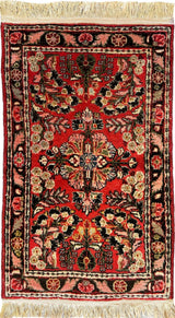 Small traditional Sarouk rug with a central floral medallion, red background, intricate black and beige floral patterns, and beige fringe on both ends.
