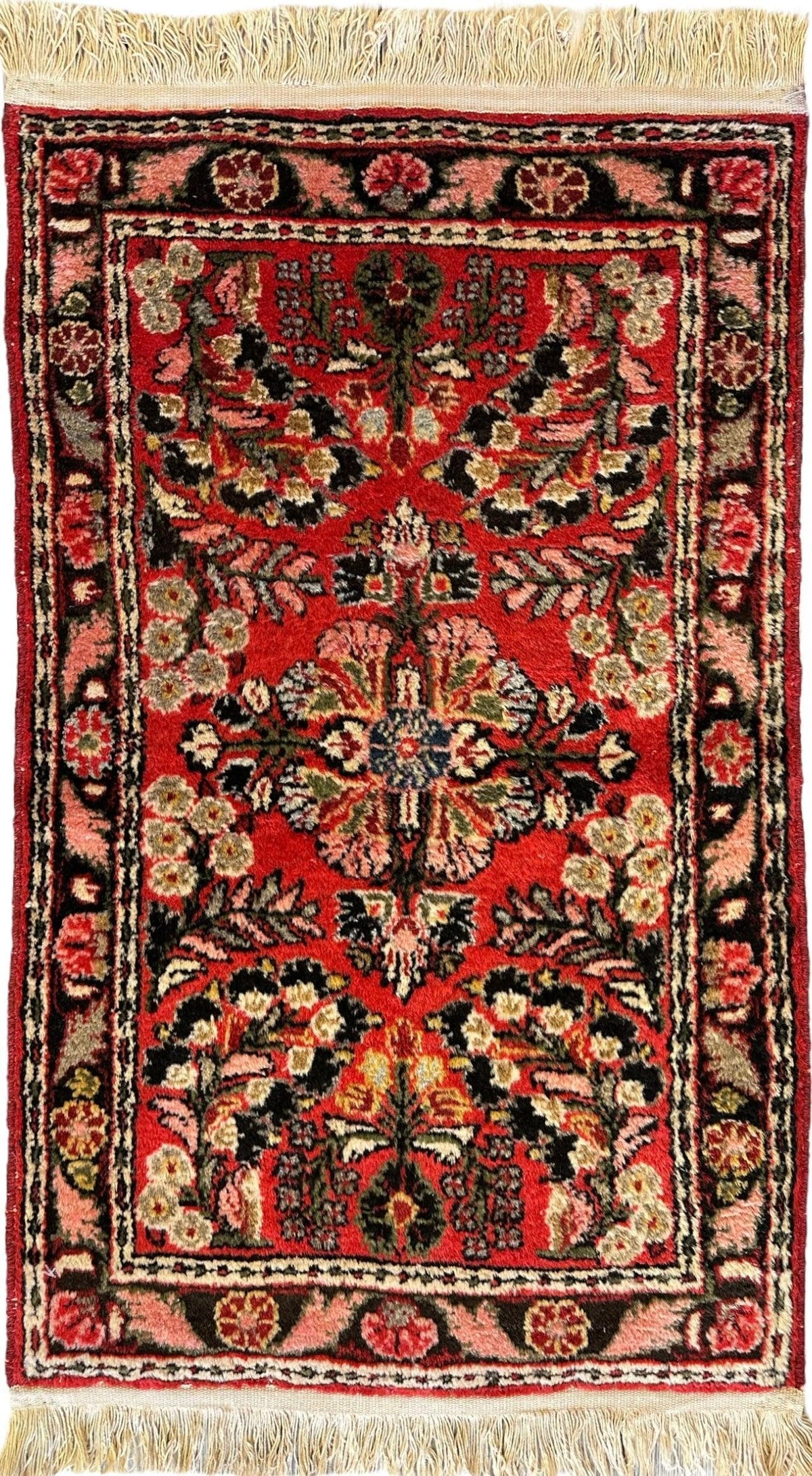 Small traditional Sarouk rug with a central floral medallion, red background, intricate black and beige floral patterns, and beige fringe on both ends.