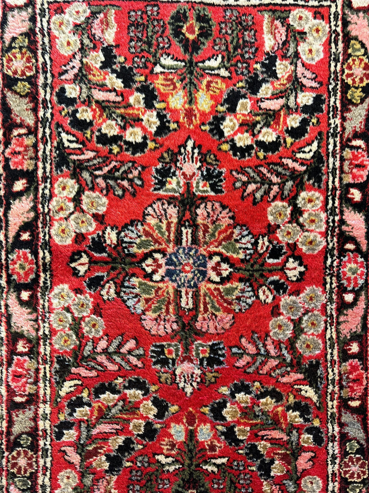 Small Sarouk rug section with red background, floral motifs in beige, black, cream, and blue, framed by intricate black and pink borders.