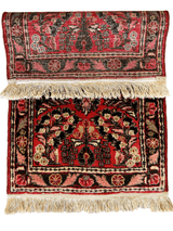 Small rectangular Sarouk rug featuring intricate floral patterns in red, black, and beige, with fringed edges on both ends, displayed partially rolled.