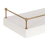 Close-up of a white rectangular floating shelf with thin brass railings on two opposite corners featuring round finials and a smooth finish