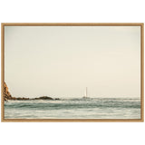 Sailboat with white sails on calm blue ocean near rocky shore under a pale sky with distant birds flying