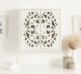 White wall-mounted wooden cabinet with intricate circular floral carvings on double doors, set against a white wall above a shelf with neutral-toned decor.