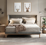 Modern bedroom with grey upholstered bed featuring neutral bedding and pillows, flanked by round wooden side tables with lamps, and two framed deer head prints above.