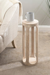Tall, cylindrical Dahl wood drink table with vertical open slats topped by a light gray ceramic mug, positioned next to a beige upholstered couch on a textured floor.