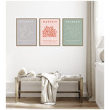 Three framed minimalist art prints above a wooden bench with an open book and draped fabric; prints feature a white dove on gray, red coral on pink, and abstract dancers on muted green.