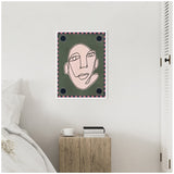 Framed abstract line drawing of a face with a pink oval shape on an olive green background, bordered by alternating pink and dark squares and four sun motifs, hanging above a bedside table with books and a cup.