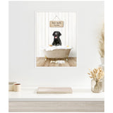 Black Labrador sitting in a beige clawfoot bathtub filled with white bubbles, under a wooden sign reading 'Hot Bath $1.00' against white vertical panel walls and wooden floor.
