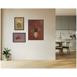 Three framed artworks on a beige wall: a pink cyclamen with green leaves on tan background, a still life of fruit on purple background, and a floral bouquet in a cream vase on dark red background.