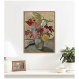Framed canvas wall art of a colorful bouquet with red, pink, yellow, and white flowers in a gray vase against a muted background hung above a white surface with a lamp, photo frame, and potted plant.