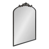 Rectangular mirror with an arched top, framed in dark metal featuring an ornate floral and scrollwork crest at the arch's peak.