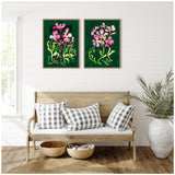 Two framed canvases with pink floral shapes on dark green backgrounds hang above a wooden bench with plaid cushions, beside a large white planter with green foliage.