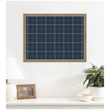 Rectangular wall-mounted fabric pinboard with navy blue and tan plaid pattern in a light wooden frame above a white console holding a lamp, photo frame, plant, and bowl.