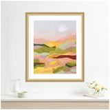 Abstract landscape painting featuring layered blocks of soft pink, yellow, green, and brown hues under a pale circular sun in a light beige frame on a white wall.