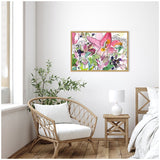 Framed canvas with loose, colorful floral painting in pinks, greens, and purples hanging above a rattan chair with white cushions in a bright, minimalist room.