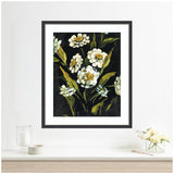 Framed floral artwork depicting white and yellow flowers with green leaves against a deep black background, hanging on a white wall above a minimalist shelf.