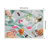 Overhead view of a poker game on a light teal satin cloth featuring pink poker chips, playing cards, drinks, cigars, cherries, and a stack of cash, highlighted by hands with rings.