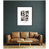 Abstract floral artwork in black and beige tones framed in black, hanging above a brown leather sofa with a pillow, behind a wooden coffee table with glass vases.