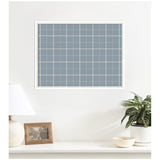 Light blue plaid fabric pinboard with white grid lines in a white frame mounted on a white wall above a shelf with a white lamp, framed photo, potted plant, and bowl.