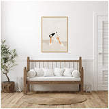 Minimalist framed art print above wooden bench with white cushions, depicting hands holding a wine bottle and glass on a beige background in a bright, serene room.