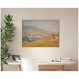 Framed canvas wall art depicting a soft, muted landscape of mountains and houses in earthy browns, greens, and blues, hanging above a wooden desk with books and a white chair.