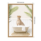 Framed canvas showing a cheetah sitting in a vintage clawfoot bathtub with white bubbles, flanked by green palm leaves against a white paneled wall.