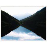 Minimalist lake reflection at sunrise with dark silhouetted mountain slopes and pale blue sky mirrored in still water, framed in white border.
