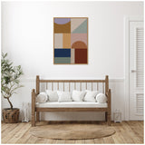 Geometric wall art with muted brown, blue, purple, and gray shapes above wooden framed bench with white cushions in bright minimalist room.