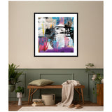Abstract wall art with layered colors including black, white, blue, pink, and purple, framed in black and displayed above a wooden bench with cushion and throw in a muted green and beige room.