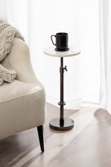 Small adjustable-height side table with round white marble top and black metal base, shown next to a cream upholstered chair with a knitted throw.