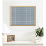 Light wood framed rectangular fabric pinboard with a light blue and white grid plaid pattern, hung on a white wall above a white surface with plant, lamp, and photo frame.