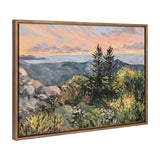 Framed landscape painting showing a sunrise over a mountainous terrain with two prominent evergreen trees and wildflowers in the foreground under a pastel sky.