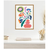 Framed canvas showing a retro floral arrangement with colorful abstract flowers in a wavy pink vase, hung on a light wall above a white desk with dried plants.