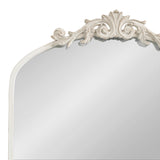 Arched mirror with an ornate cream-colored frame featuring intricate floral and scroll detailing at the top center against a white background.