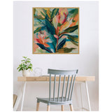 Abstract botanical canvas with vibrant green, teal, coral, and peach tropical leaves in a natural wood frame, hanging above a minimalist wooden desk and gray chair.