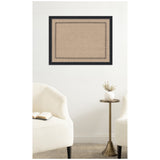 Rectangular cork pinboard with a black scallop pattern border mounted on a white wall above a small brass side table and two cream upholstered chairs.