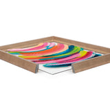 Abstract framed print with bold curved brushstrokes in pink, blue, green, yellow, and orange, set in a natural wood frame shown from a low corner angle.