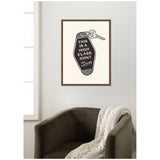 Framed black and white print with a vintage keychain illustration reading 'This is a High Class Joint' hanging above an olive green armchair draped with a cream knitted throw.