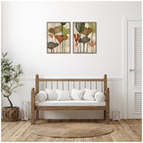Two framed canvas prints featuring abstract botanical shapes in muted earth tones, hung side by side above a wooden bench with white cushions in a minimalist room.