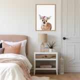 Framed canvas of a young fawn with a pink and white flower crown hanging above a white nightstand with a beige lamp and small plant in a softly lit bedroom.