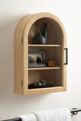 Light wood wall cabinet with rounded top, black handle, and two shelves displaying a black vase, framed photo, amber jar, and small black tray with stones and plant
