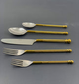 Set of five stainless steel flatware pieces with gold twisted handles and rounded ends, including two forks, a knife, and two spoons, arranged on a dark surface.